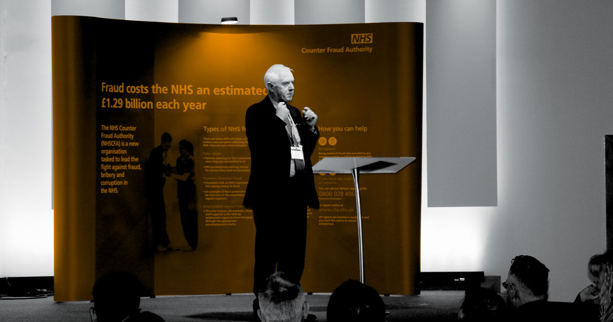 Image of Tom Taylor Chaiman of the NHSCFA Board on stage talking to an audiance