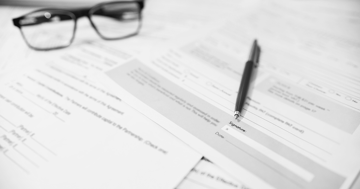 Image of glasses and a pen sitting on top of pile of forms