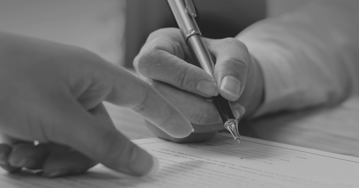 Image of two hands one is holding a pen the other is pointing to a signautre line of a form