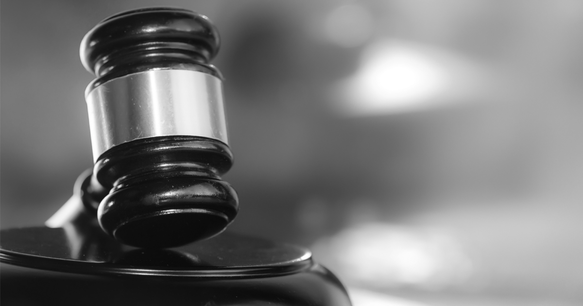 Image of a person sitting with their face in the hands, with a judge looking at them reading from a document infront of them.