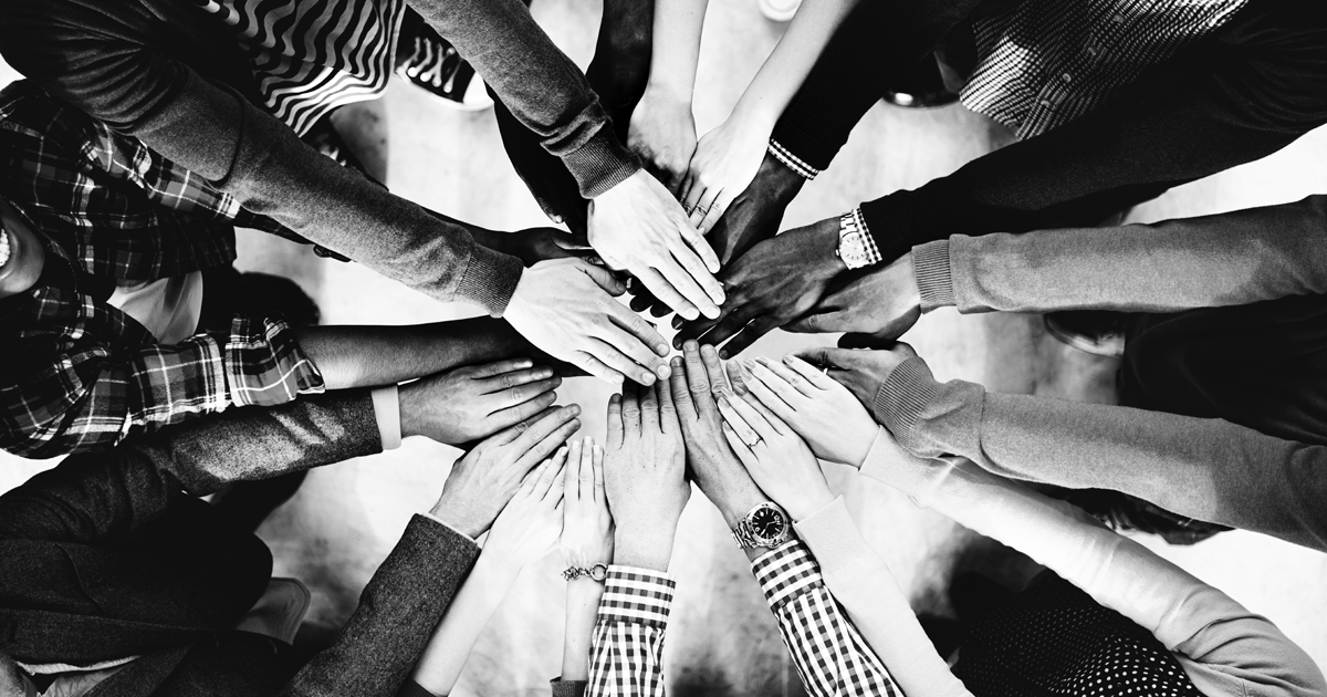 Image of group of people in a circle all putting one of their hands into the center 