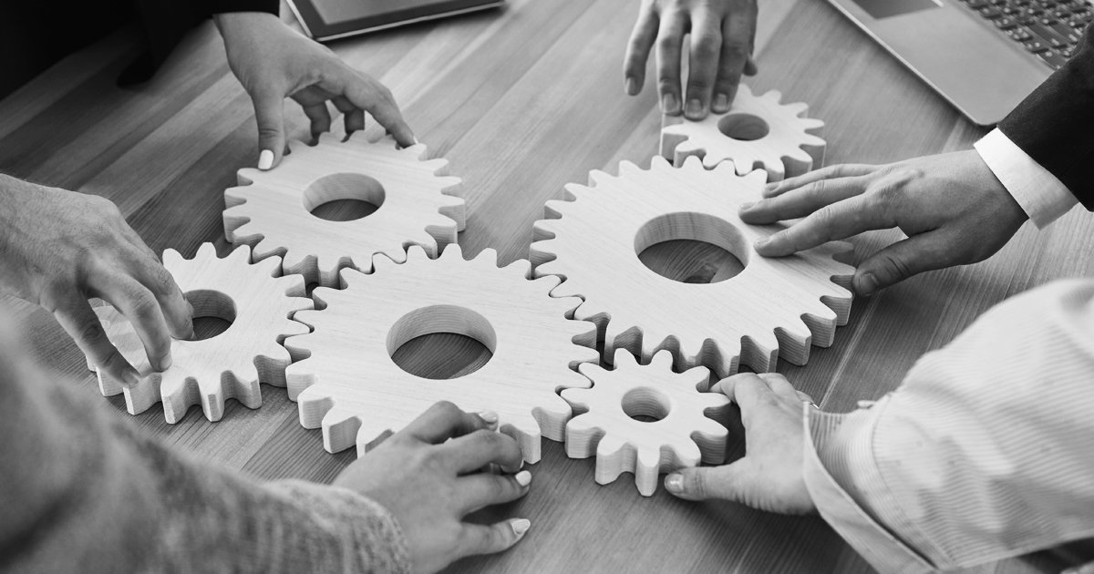 Image of six hands holding togehter a set of cogs
