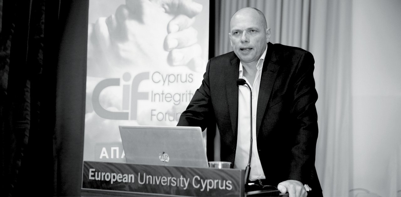 Image of Alex Rothwell talking at a lecturn with the words European University Cyprus on a small sign infornt
